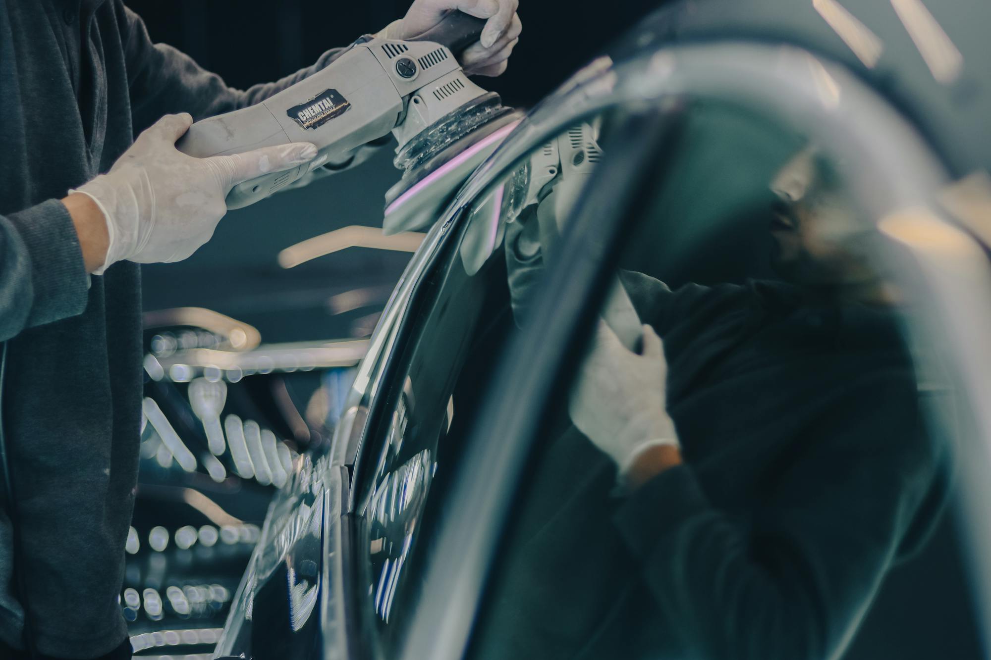A detailer using a dual-action polisher on a glossy dark vehicle panel - the paint-correction prep step that determines whether a ceramic coating actually performs as advertised.