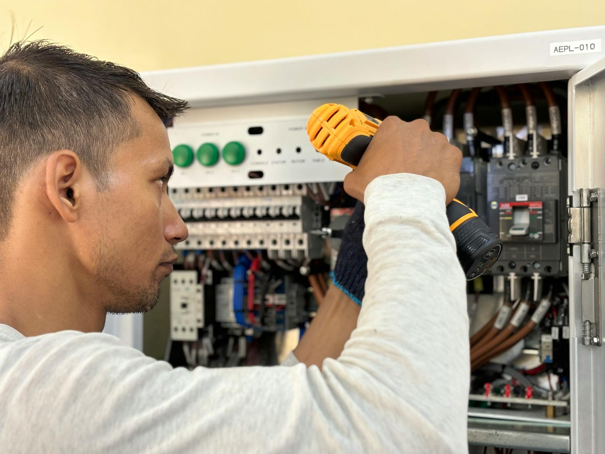 An electrician working with a power drill on a residential electrical panel during an EV charger install - the kind of code-compliant Level 2 work (NEC 625.42, 125% continuous load) that defines the $1,200-$3,000 high-margin install ticket in 2026.