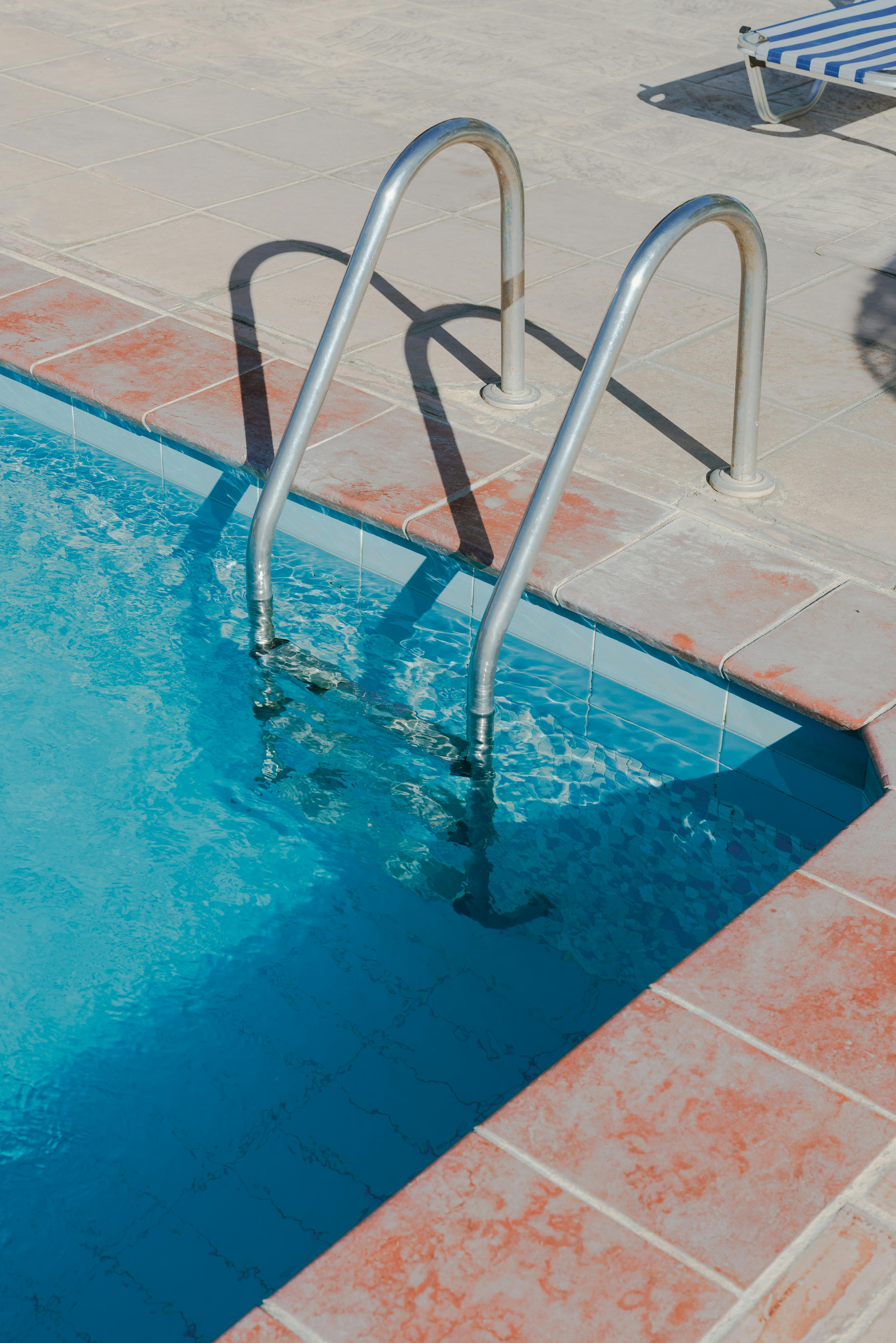 Stainless-steel pool ladder set into a tiled deck - the kind of installed pool hardware (ladders, plumbing, pumps, salt cells, heaters, automation) that drives equipment-side revenue 5-30× larger per job than chemical-only service.