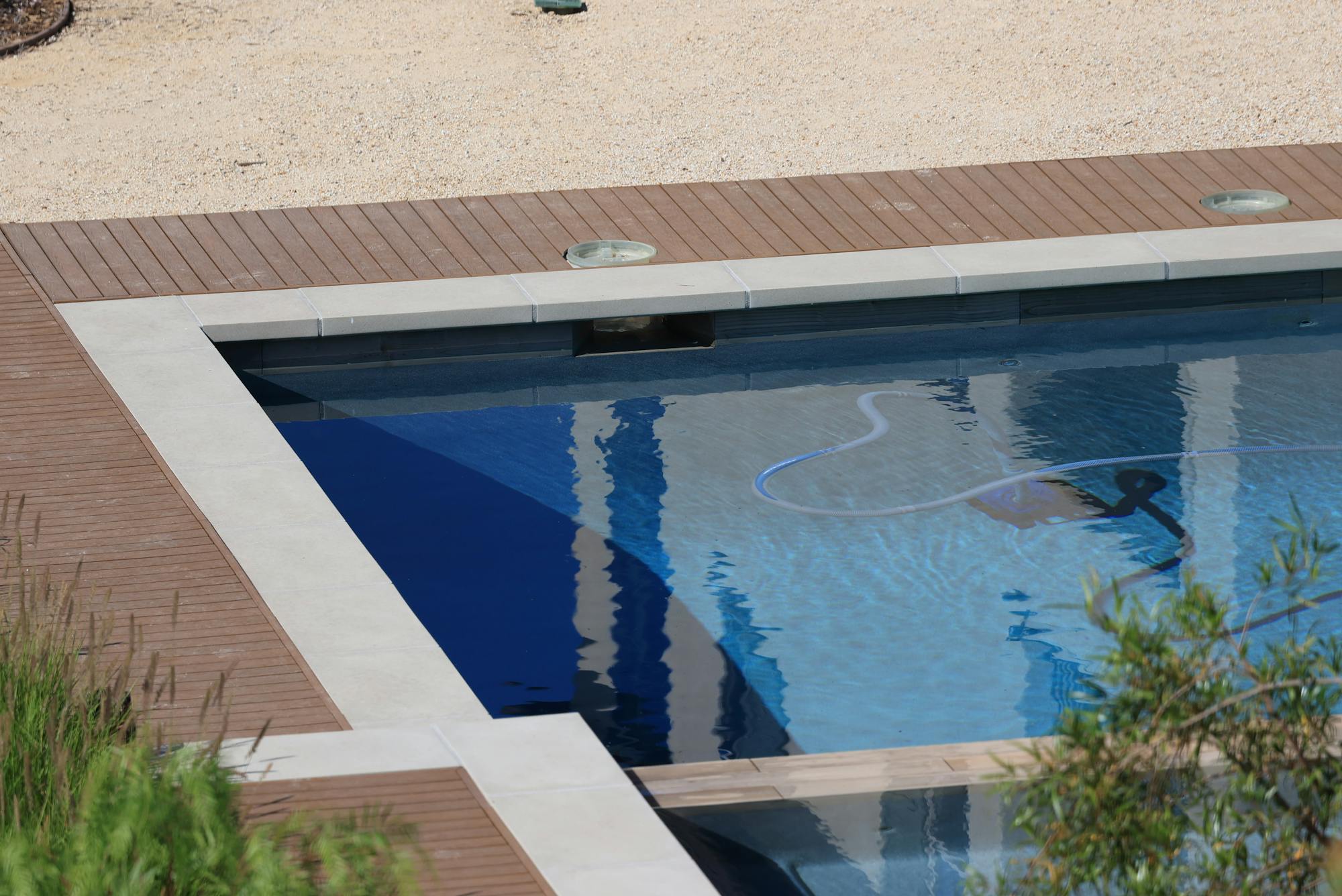 A residential swimming pool with a manual vacuum hose visible underwater during a routine service visit - the kind of weekly recurring chemical and skim work ($80-$190/mo per pool) that anchors a route-density-driven pool service business in 2026.